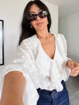 Blusa blanca con estampado de lunares, confeccionada en tela semitransparente. Presenta escote en V con volados frontales y mangas largas acampanadas con volados en los puños.