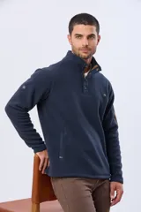 Buzo de abrigo confeccionado en tejido polar térmico, con cuello alto y cierre frontal parcial con broches. Presenta bolsillos laterales con cierre y un bolsillo adicional con cierre en la manga izquierda.