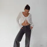 Blusa blanca traslúcida con escote en V, volados en el contorno y mangas largas acampanadas con lazos en los puños.