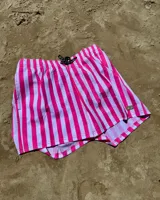 Short de baño celeste y blanco a rayas verticales, con cintura elástica ajustable con cordón negro y logo de la marca en la pierna izquierda.