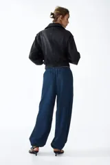 Pantalón tobillero en denim suave de corte holgado con piernas globo, cintura elástica y bolsillos laterales discretos, con abertura ajustable mediante cordón en los bajos.