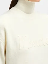 Buzo de lana y cachemira color crema, con cuello alto y logo de la marca bordado en el frente.