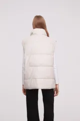 Chaleco acolchado color marfil con cuello alto y cierre frontal con botones a presión.