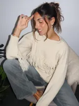 Sweater tejido a mano en lana merino, color crudo, con cuello a la base, mangas holgadas y detalle de flecos aplicados en el frente y las mangas.