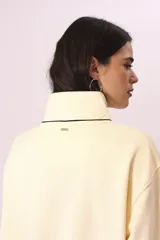 Buzo color crema con cuello alto abotonado y puños con ribete negro.