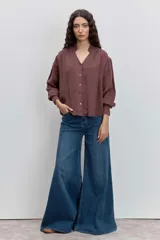 Camisa de color marrón con cuello con volados, cierre frontal con botones y mangas largas con puños elásticos.