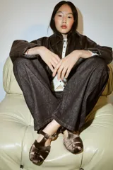 Sandalia plana estilo cangrejera con acabado efecto terciopelo en color marrón. Presenta diseño de tiras cruzadas, cierre mediante hebilla metálica lateral y punta redonda.