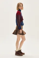 Polera de tejido de punto con diseño multicolor que combina rayas horizontales en tonos azul y bordó, flecos decorativos en el frente y un bordado central en forma de trenza. Presenta cuello semi polera, mangas largas y puños acanalados.