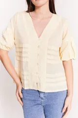 Blusa color crema con escote en V, mangas abullonadas cortas y tablas en el torso.