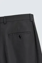 Pantalón de traje regular fit confeccionado en popelín de algodón. Presenta cintura con pliegues frontales, bolsillos laterales y bolsillos traseros de vivo con botón. El bajo tiene acabado con vuelta y el cierre es frontal con cremallera y botón.