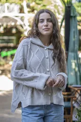 Saco tejido de punto con diseño de ochos y trenzas, color negro. Presenta cuello estilo camisero, cierre frontal con botones tipo joya, mangas holgadas y silueta oversize.