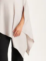 Poncho tejido de punto con diseño asimétrico y aberturas laterales para los brazos.