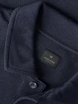 Buzo azul marino de manga larga con cuello polo y cierre frontal de tres botones. Presenta un pequeño parche cuadrado en el pecho y puños y dobladillo acanalados.