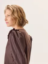 Camisa de color marrón con diseño combinado, presentando mangas abullonadas con volados en los hombros y cuerpo de algodón. Combina una textura de tela de camisa en mangas y delantero con una espalda de tejido elástico.