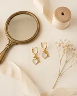 Aros tipo argolla en acero dorado con dije colgante que combina un delfín y un corazón con incrustación de nácar.