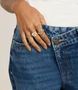 Kit de seis anillos dorados de metal reciclado. Incluye un anillo con forma de corazón esmaltado en blanco con un diseño de moño, un anillo con forma de onda, y cuatro anillos finos con detalles texturizados.