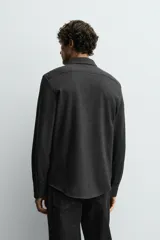 Camisa de corte relajado confeccionada en tejido de algodón con textura. Presenta cuello italiano, manga larga con puños abotonados y cierre frontal mediante botonadura.