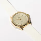 Reloj de pulsera con caja dorada, esfera color crema con agujas doradas y correa de silicona blanca con textura.