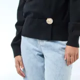 Sweater de punto negro con diseño cruzado tipo cárdigan, escote en V profundo y cierre lateral con un botón decorativo grande de efecto carey. Presenta mangas largas con puños ajustados.