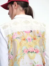 Camisa blanca de corte clásico con bordados florales en los hombros y detalles decorativos en los bolsillos frontales. Cuenta con cierre de botones y mangas largas.