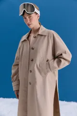 Trench midi de color camel, confeccionado en una mezcla de algodón y nylon con propiedades repelentes al agua. Presenta un diseño clásico con cuello camisero, cierre frontal de botones, bolsillos laterales y tajos en los costados.