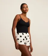Conjunto de pijama de dos piezas de la marca Lov, compuesto por una musculosa negra de tejido acanalado con escote en V y detalles de encaje, y un short blanco con estampado de lunares negros y cintura elástica.