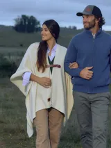 Ruana de color crudo con diseño abierto, confeccionada en tejido suave, presenta un cierre frontal mediante una hebilla de cuero marrón ajustable.