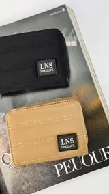 Billetera corta de diseño capitoneado con cierre perimetral y solapa frontal. Cuenta con compartimentos internos para tarjetas y billetes, e incluye una correa de mano desmontable.