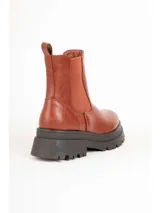 Bota de caña baja tipo Chelsea color marrón, con paneles elásticos laterales y suela track negra con plataforma dentada. Presenta textura en relieve en la parte trasera del talón.
