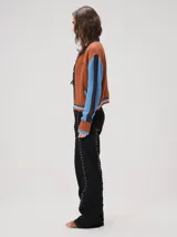 Campera estilo bomber Mutma Satifo, de diseño colorblock con cuerpo en color óxido y mangas celestes con detalles en azul marino. Cuenta con cuello camisero, cierre frontal, puños y ruedo elásticos rayados, y un parche gráfico en el pecho.
