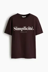 Remera marrón oscuro de algodón con cuello redondo, mangas cortas y estampa frontal en color blanco con las leyendas "Simplicité." y "Douceur de Vivre".
