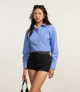 Camisa celeste con rayas verticales blancas, de corte alargado, cuello inglés y mangas largas.