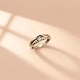 Anillo bicolor de plata y oro, con una circonia central transparente y diseño de doble banda superior.