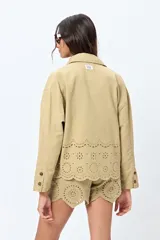 Sobrecamisa blanca de corte recto con cuello clásico, cierre frontal de botones y bolsillos delanteros. Presenta un delicado detalle de bordado inglés en el ruedo.