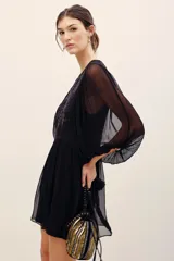 Vestido corto negro con transparencias, mangas largas amplias y detalles de bordados florales con lentejuelas en el frente. Cuenta con un lazo ajustable en la cintura y falda fluida.