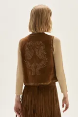 Chaleco de cuero color camel con bordados decorativos, tachas metálicas en los bordes y cierre frontal mediante lazos.