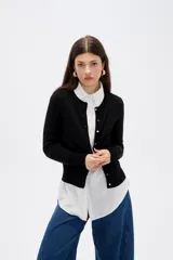 Saco de punto al cuerpo, color negro, con cuello redondo, manga larga y cierre frontal con botones pequeños.