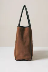 Bolso tipo tote de gamuza color marrón con detalles de bordes y asas en cuero negro.