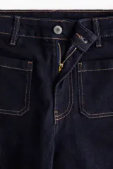Jean de denim azul oscuro con tiro alto y corte wide leg de pierna amplia. Presenta bolsillos delanteros tipo parche con costuras pespuntadas en contraste y cierre frontal con botón y cremallera.