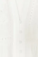 Blusa blanca de manga larga con escote en pico y cuello redondo. Cuenta con bordados florales frontales a tono, puños con volados y cierre frontal de botones.