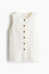 Chaleco sin mangas de punto fino color blanco, con escote redondo y botonadura frontal de botones marrones. Presenta bolsillos delanteros falsos.