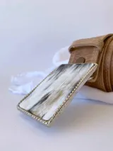 Cinto de cuero color camel con forro de cuero y hebilla rectangular de guampa con borde metálico trenzado. Cuenta con broche suizo intercambiable.