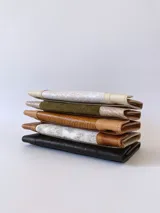 Billetera de cuero negro con sistema de cierre con broche y monedero externo. Presenta un diseño texturizado en la solapa frontal.