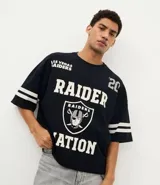 Remera deportiva de corte oversized, color negro, con estampado gráfico en la espalda del equipo Las Vegas Raiders de la NFL. Presenta cuello redondo, mangas cortas con detalles de rayas blancas y logo de la NFL en la parte superior trasera.