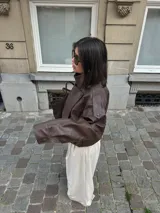 Chaqueta de efecto cuero con cuello alto, cierre frontal cruzado con botones a presión, hombreras y cintura elástica. Presenta un acabado texturizado y bolsillos laterales.