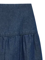 Pollera corta de denim azul medio, con tiro medio y cierre de cremallera. Presenta un diseño con un volante fruncido en el ruedo.