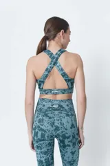 Top deportivo de lycra color verde con estampado abstracto en tonos verde oscuro y celeste. Espalda cruzada y compresión alta.