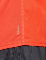 Remera deportiva Adidas de manga larga, color naranja, con cuello redondo y logo reflectante en el pecho. Presenta las icónicas tres tiras en la manga izquierda.