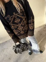 Buzo de tejido de punto grueso en color verde oliva con diseño jacquard en tonos grises y blancos. Presenta cuello redondo, mangas largas y terminaciones acanaladas en puños y ruedo.
