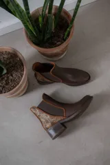 Botinetas de cuero color marrón con diseño tipo chelsea, con paneles laterales elásticos y detalle de cuero texturizado con acabado metalizado en el talón. Poseen taco bajo cuadrado y terminación redondeada.